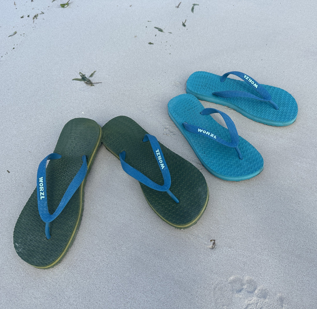 2 pairs of Worzl flip flops on a beach depicting comfort and durability of the natural rubber flip flops.
